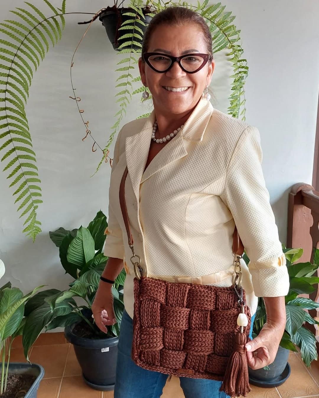 Cliente de blazer claro com a bolsa Atenas marrom a tiracolo, numa varanda com plantas