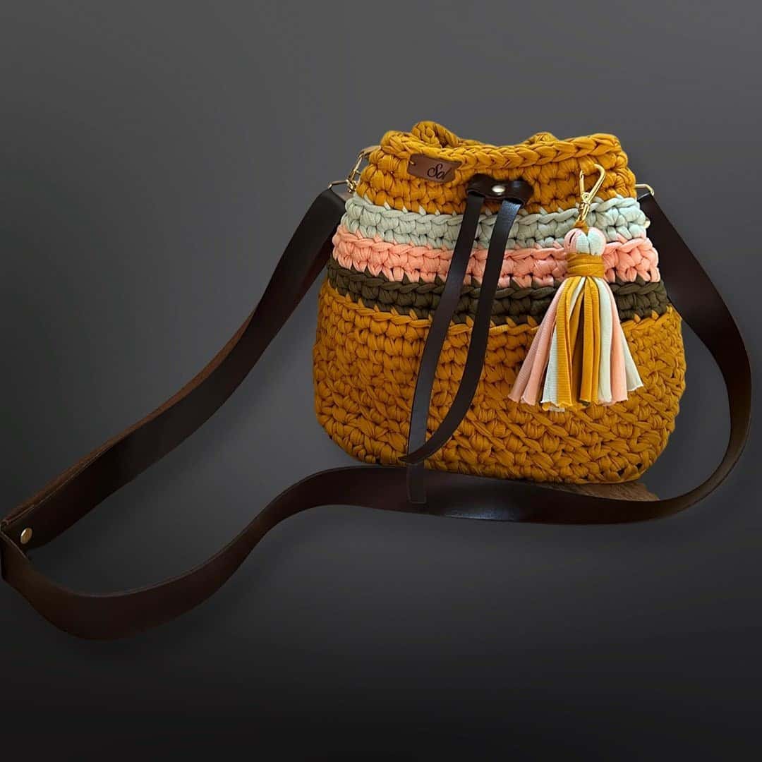 Bolsa saco Viena Mini mostarda com listras coloridas, tassel e alça tipo couro marrom